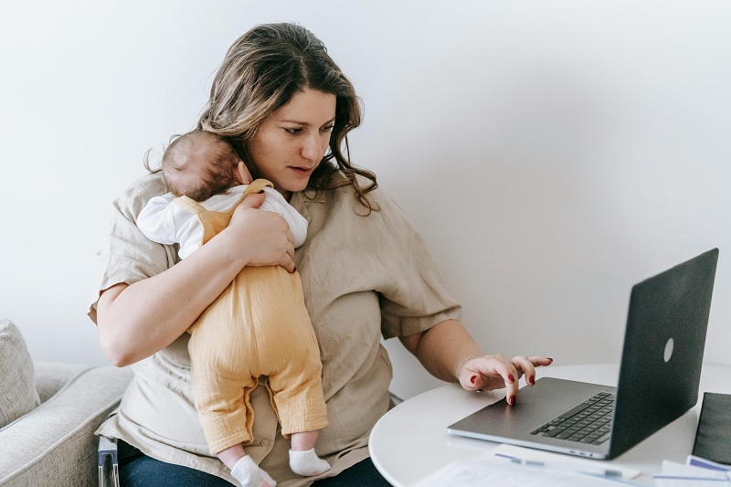 a mom has a baby in her shoulder and working on laptop